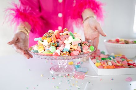 Female entrepreneur smiling while holding a tray of rainbow-colored candies in a stylish Vancouver studio, radiating energy and enthusiasm.