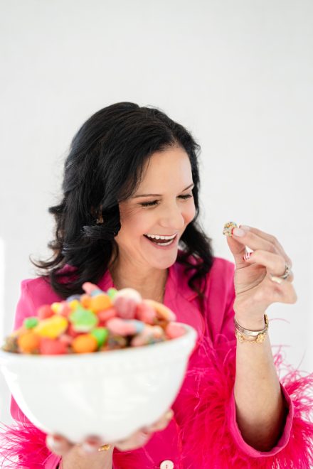 Playful female entrepreneur surrounded by colorful candies in a bright Vancouver studio, showcasing her vibrant candy brand.