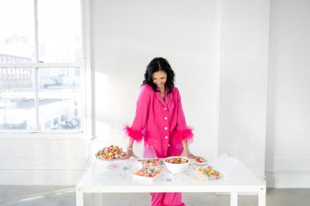 Female entrepreneur smiling while holding a tray of rainbow-colored candies in a stylish Vancouver studio, radiating energy and enthusiasm.