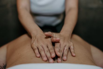 Hands of a massage therapist gently adjusting a client’s shoulder in a calming Fraser Valley treatment room, showcasing expertise and trust.