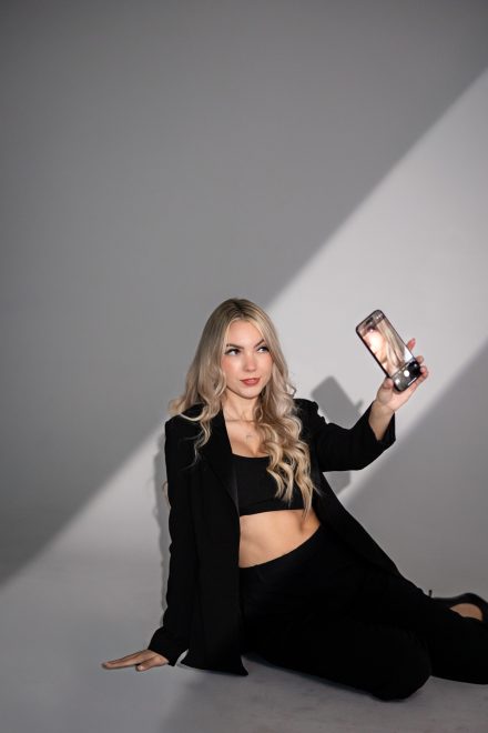 Demi sitting confidently holding her phone, captured in a dramatic, high-contrast branding portrait in Port Coquitlam.